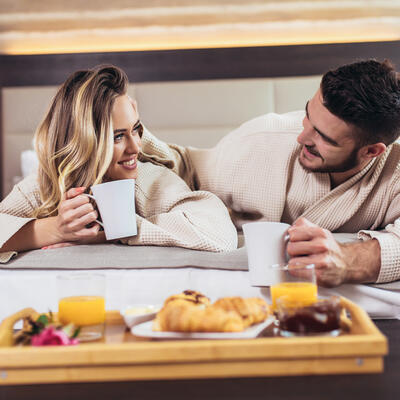 Smiling couple having breakfast in bed in hotel room