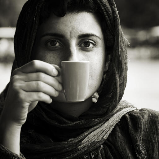 Frau mit Kopftuch hlt sich eine Tasse vor den Mund