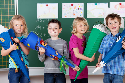 Kinder mit Zuckertten zur Einschulung vor einer Tafel