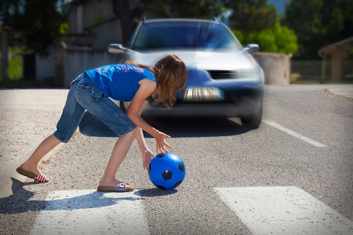 Spielendes Kind mit Ball im Straßenverkehr vor einem herannahenden Auto