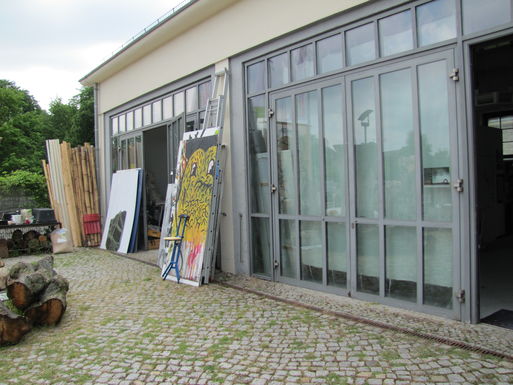 Bild vergrößern: Eingangsbereich mit lichtoffenen Fenstern und angelehnten Gemälden am Künstleratelier
