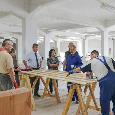 Ein Projektteilnehmer lasiert Holzteile im Beisein der Besuchergruppe