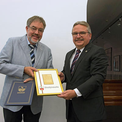 Bürgermeister Klaus Zimmermann und Prof. Dr. Detlef Siemen präsentieren die goldene Stadtplakette. 