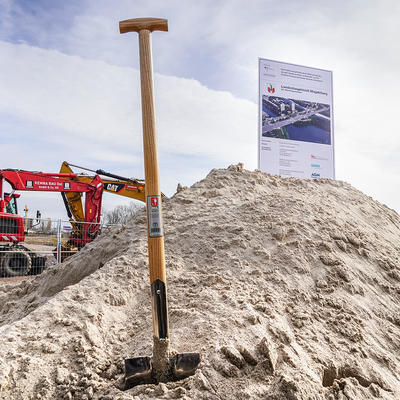 Spaten im Sandhaufen vor Baugroßgeräten für den neuen Strombrückenzug