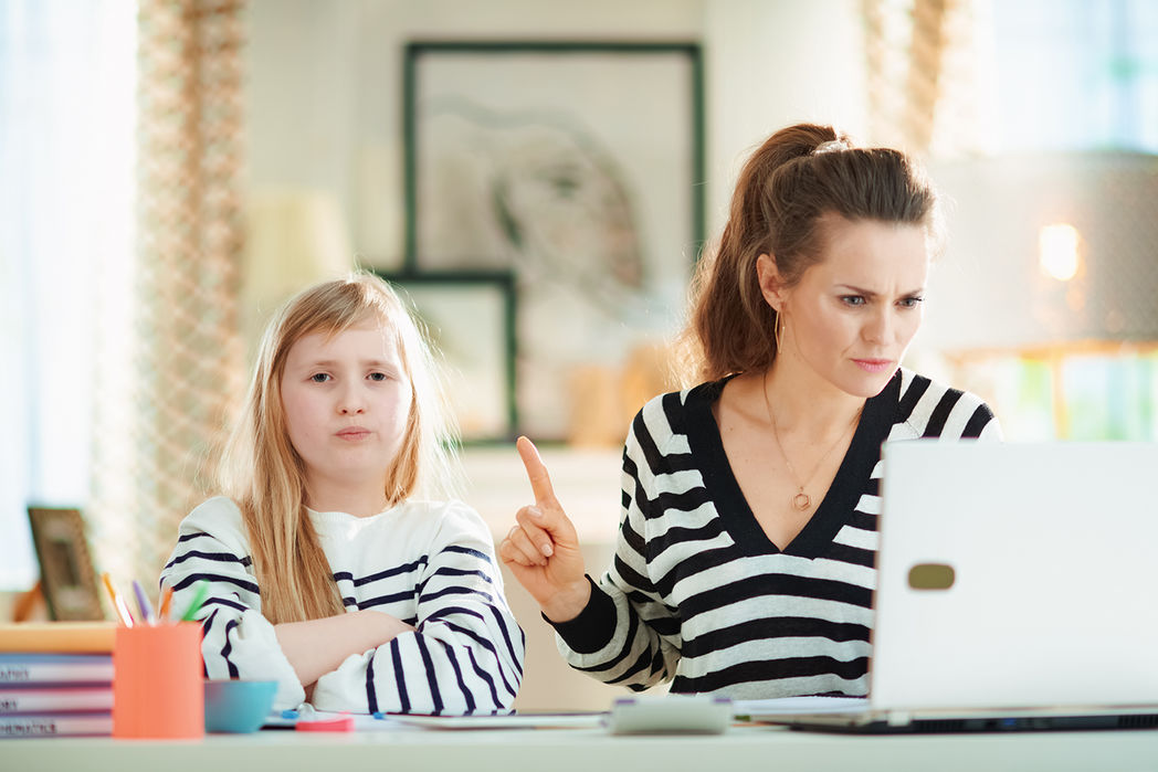 Erziehende vor einem Laptop mit gehobenem Zeigefinger in Richtung Kind © Alliance - stock.adobe.com