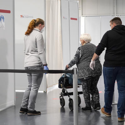 Ein Helfer und eine Helferin unterstützen eine Frau im Impfzentrum Magdeburg