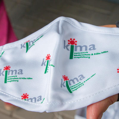 Kindergerechte Mund-Nasen-Bedeckung mit dem KiMa-Logo