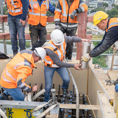 Bauarbeiter geben die Zeitkapsel mit einem Käfig aus Armierungen in den Beton