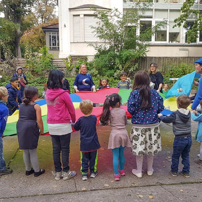 Kinder unterschiedlicher Ethnien spielen mit einem bunten Stoffsegel