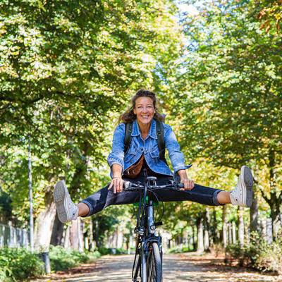 Eine Radfahrerin fährt mit ausgestreckten Beinen eine Allee