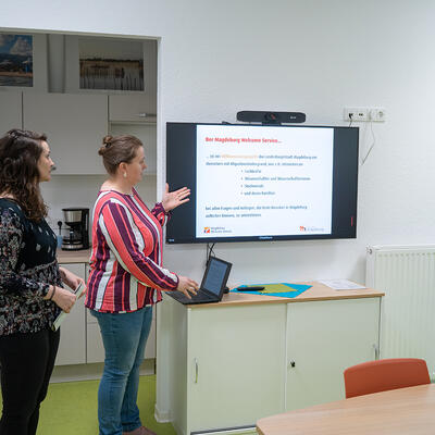 Mitarbeiterinnen des Magdeburg Welcome Service vor einem Präsentatiosnbildschirm