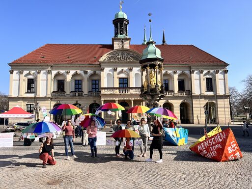 Bild vergrößern: Menschen halten bunten Regenschirm vor dem Rathaus