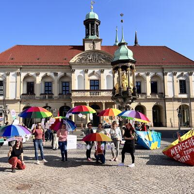 Bild vergrößern: Menschen halten bunten Regenschirm vor dem Rathaus