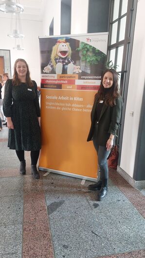 Bild vergrößern: Annika Felske und Christin Rose im Rathaus neben dem Aufsteller Soziale Arbeit in Kitas