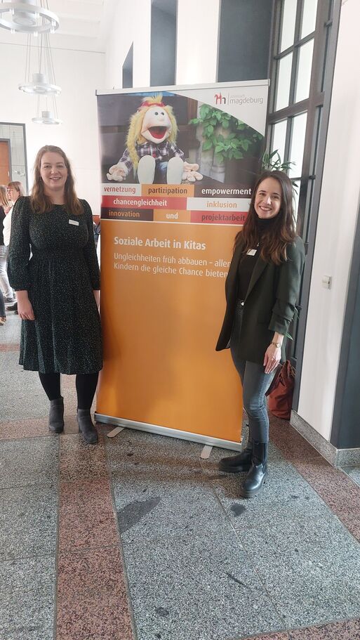 Bild vergrößern: Annika Felske und Christin Rose im Rathaus neben dem Aufsteller Soziale Arbeit in Kitas